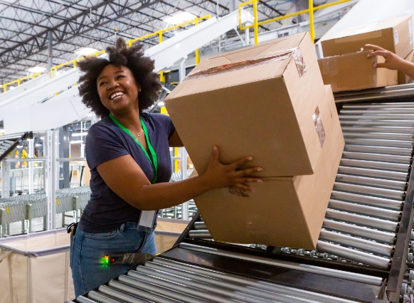 Warehouse worker smiling as she grabs boxes off a conveyor belt